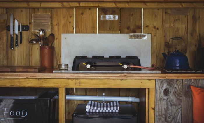 A campfire kitchen with a gas hob, kettle, chefs knives, tea making equipment, a fridge and tea towels.
